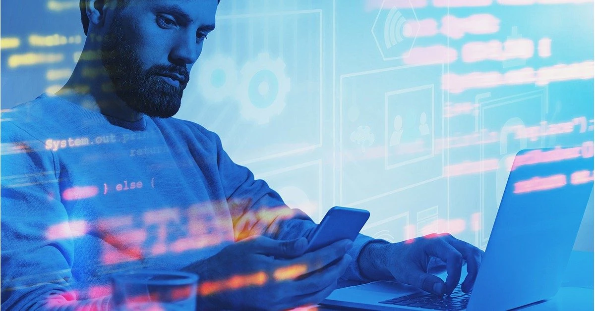 A man is working with his computer and phone